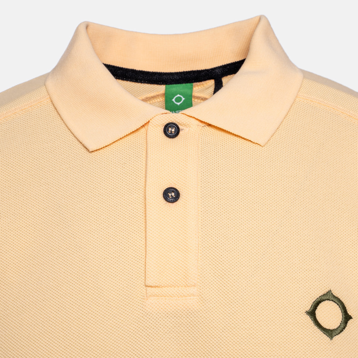 Close-up of a light peach-pink polo shirt with a black collar trim, two black buttons, and a small black geometric logo on the left chest. MA.Strum Polo available at Sakks Menswear in Southampton.