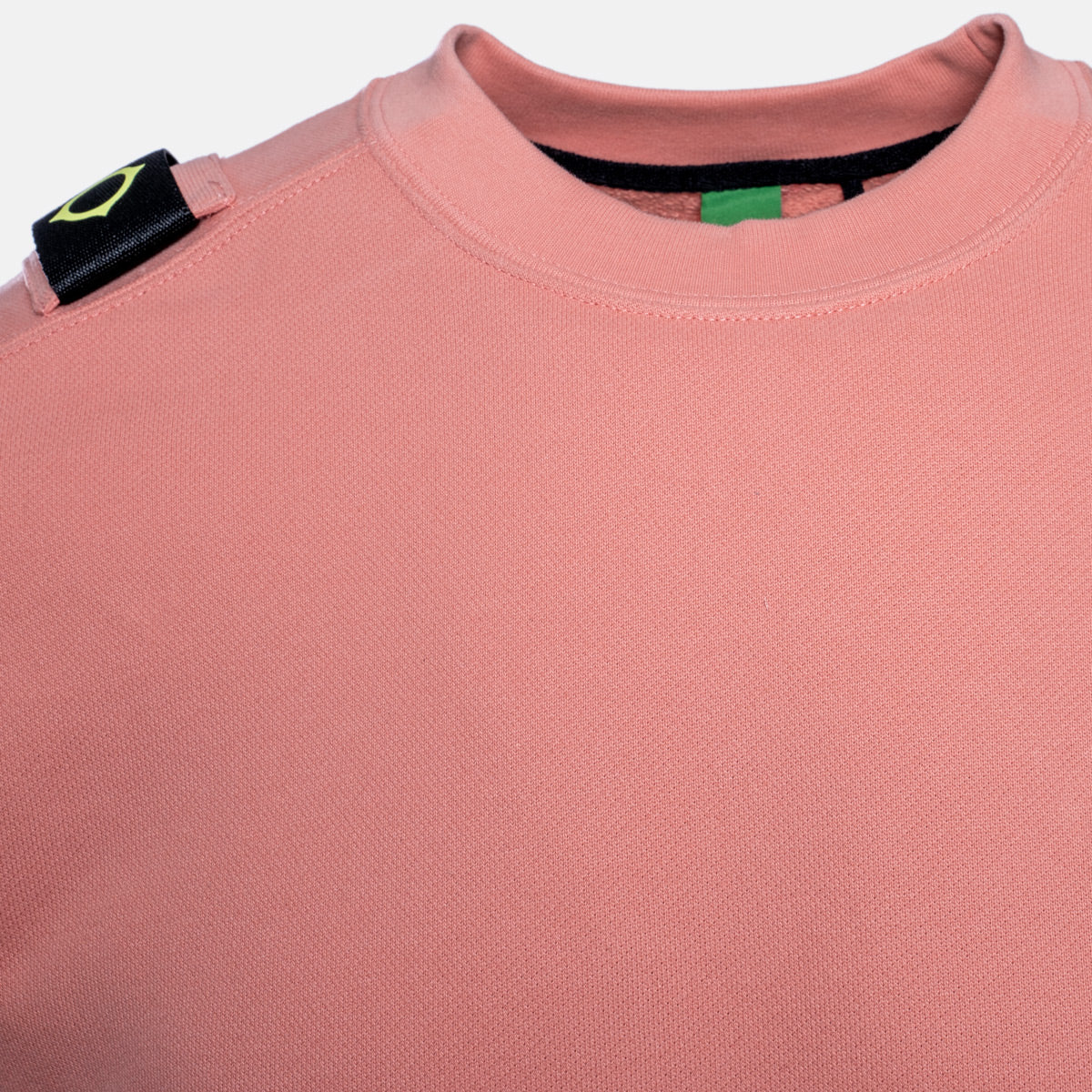 Close-up of a dusty pink crewneck sweatshirt, showing the textured fabric, a black shoulder patch with a yellow-green logo, and the inner collar. MA.Strum Sweatshirt available at Sakks Menswear in Southampton.