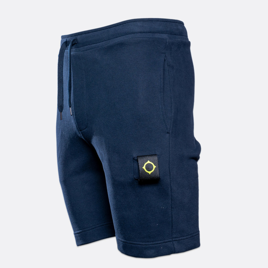 A pair of navy blue sweat shorts with a drawstring waist and a small black brand patch on the left leg, shown against a light gray background. MA.Strum Sweat Shorts available at Sakks Menswear in Southampton.