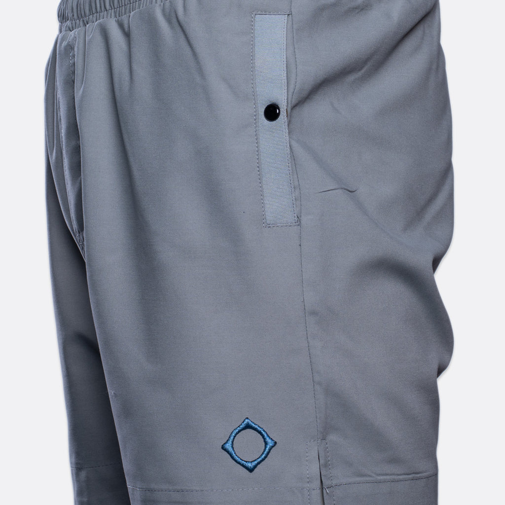 Close-up of gray athletic shorts with an elastic waistband, a vertical zip pocket with a black snap, and a blue embroidered geometric logo near the lower left leg. MA.Strum Swimwear available at Sakks Menswear in Southampton.