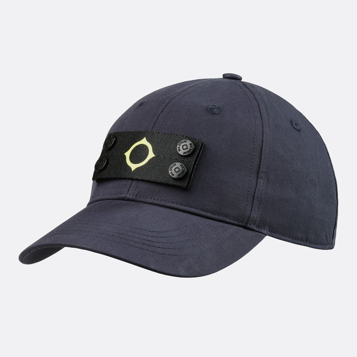 A dark navy blue baseball cap featuring a black adjustable strap across the front with a gold geometric logo and two silver buttons. MA.Strum Cap available at Sakks Menswear in Southampton.