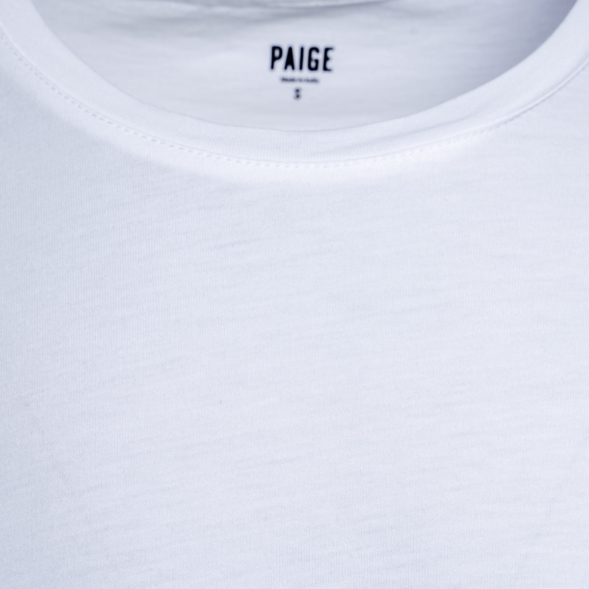 Close-up of a white crew-neck t-shirt showing the inner neck label with the brand name PAIGE. PAIGE T-Shirt available at Sakks Menswear in Southampton.