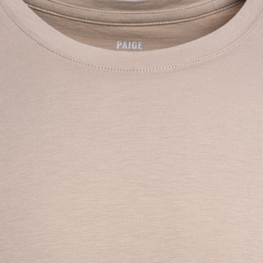 Close-up of a beige crewneck t-shirt with the brand name 'PAIGE' printed inside the collar. PAIGE T-Shirt available at Sakks Menswear in Southampton.