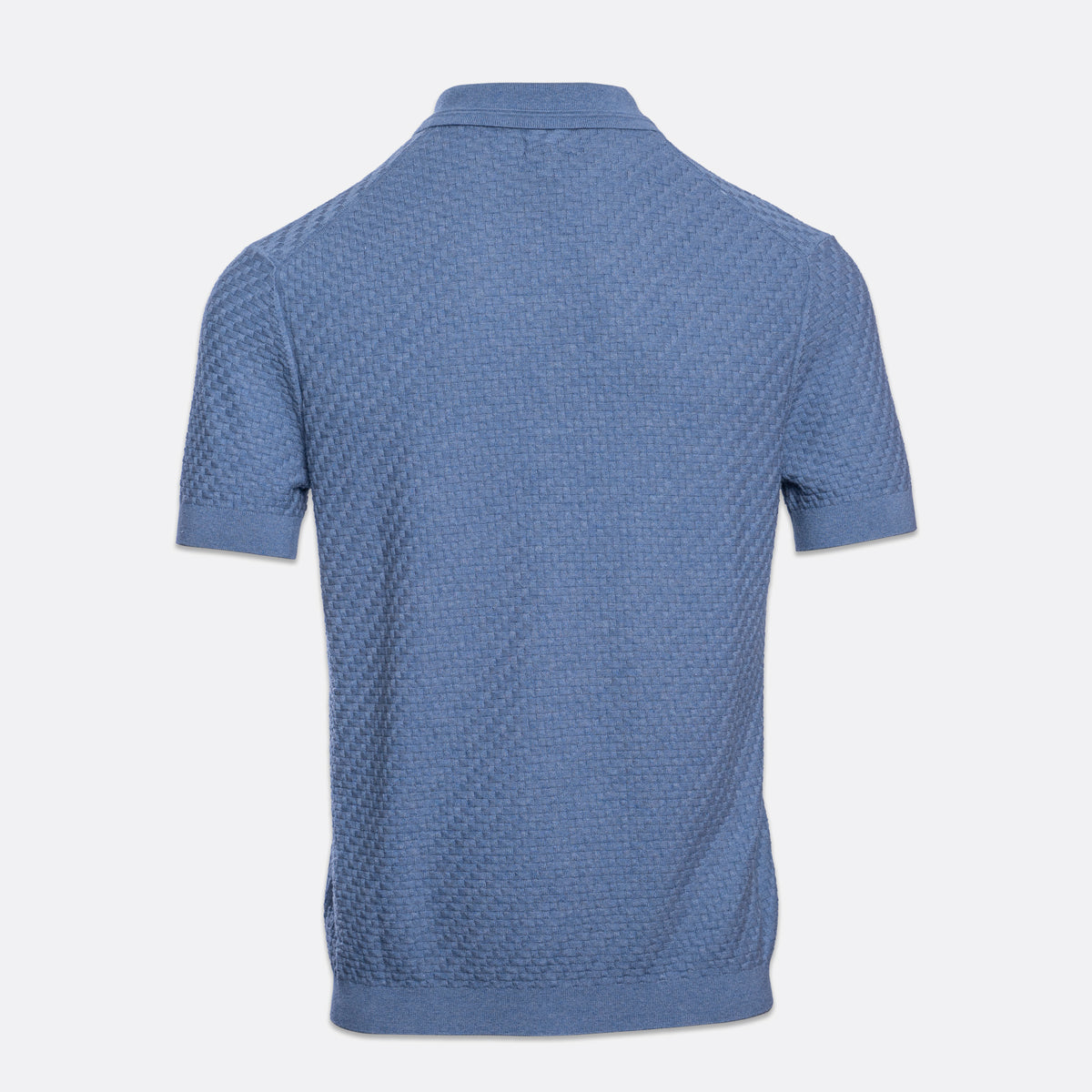 A short-sleeve polo shirt in a dusty medium blue color, shown from the back. The shirt features a textured, waffle-like knit pattern and a classic collar, displayed on a clean, light gray background. PAIGE Polo available at Sakks Menswear in Southampton.