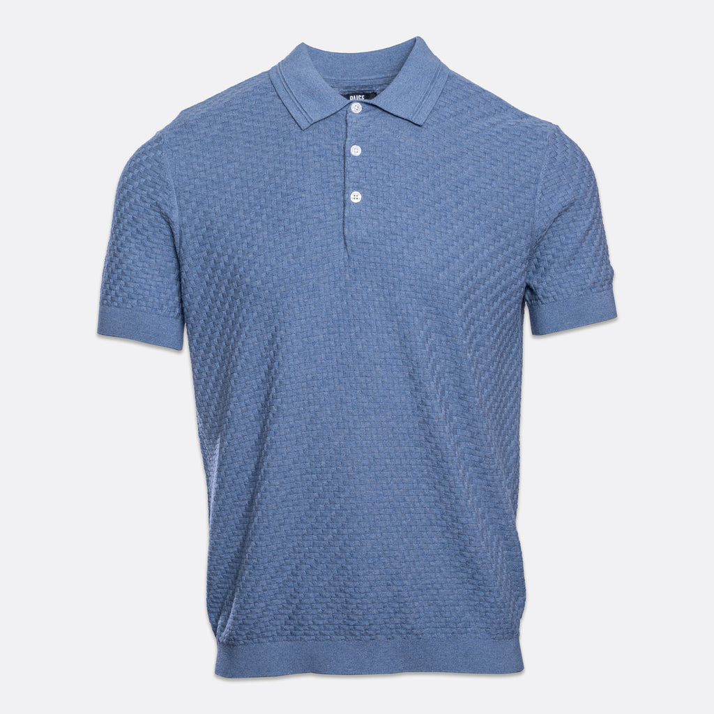 A short-sleeve polo shirt in a textured blue fabric, featuring a two-button placket and white buttons, displayed on a light gray background. PAIGE Polo available at Sakks Menswear in Southampton.