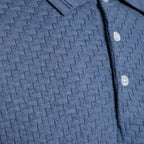 Close-up of a textured blue knit polo shirt with a buttoned collar and white buttons. PAIGE Polo available at Sakks Menswear in Southampton.