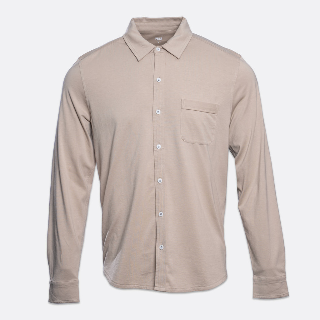 A long-sleeve button-up shirt in a light taupe-beige color, featuring a pointed collar, a single chest pocket, and white buttons, shown against a light gray background. PAIGE Shirt available at Sakks Menswear in Southampton.