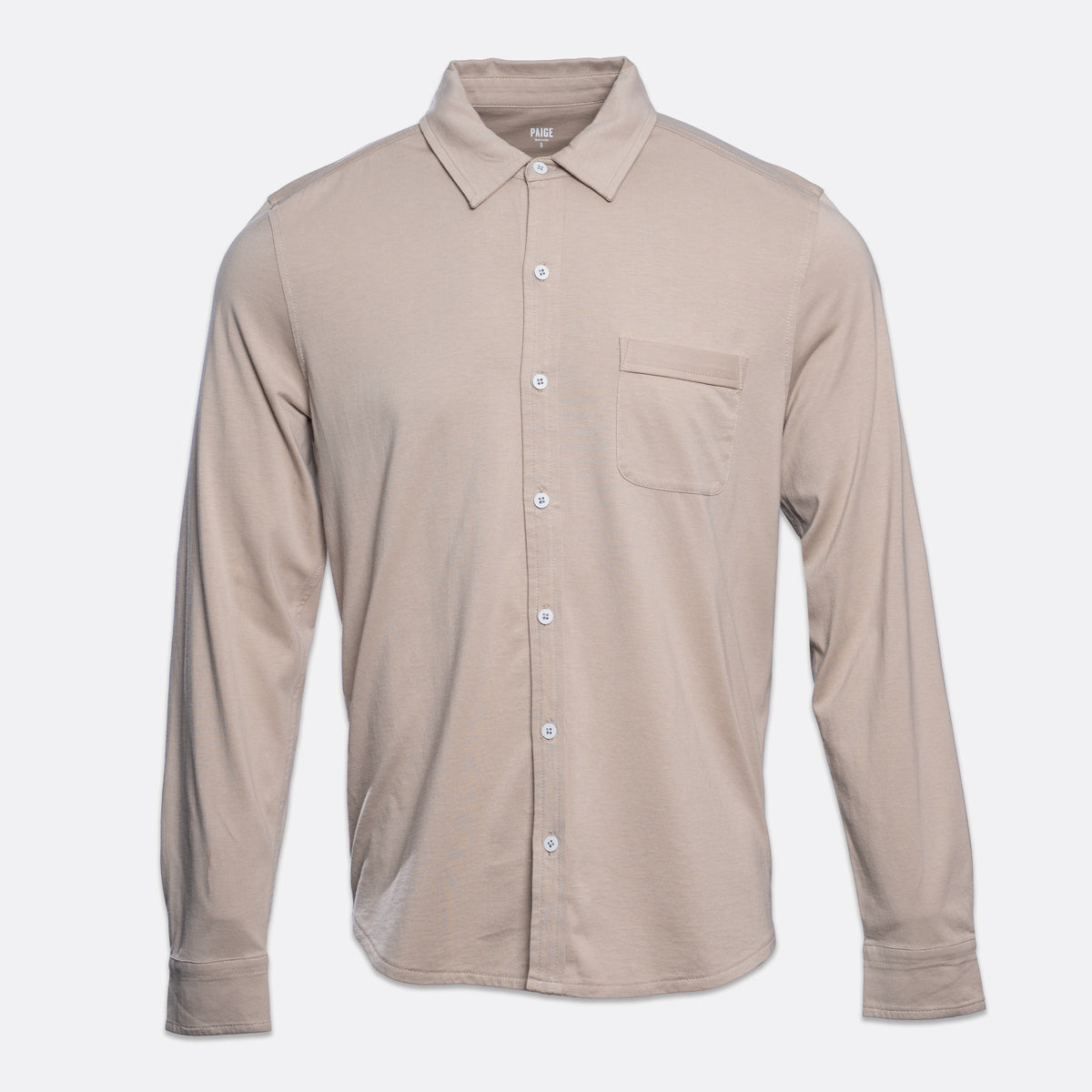 A long-sleeve button-up shirt in a light taupe-beige color, featuring a pointed collar, a single chest pocket, and white buttons, shown against a light gray background. PAIGE Shirt available at Sakks Menswear in Southampton.