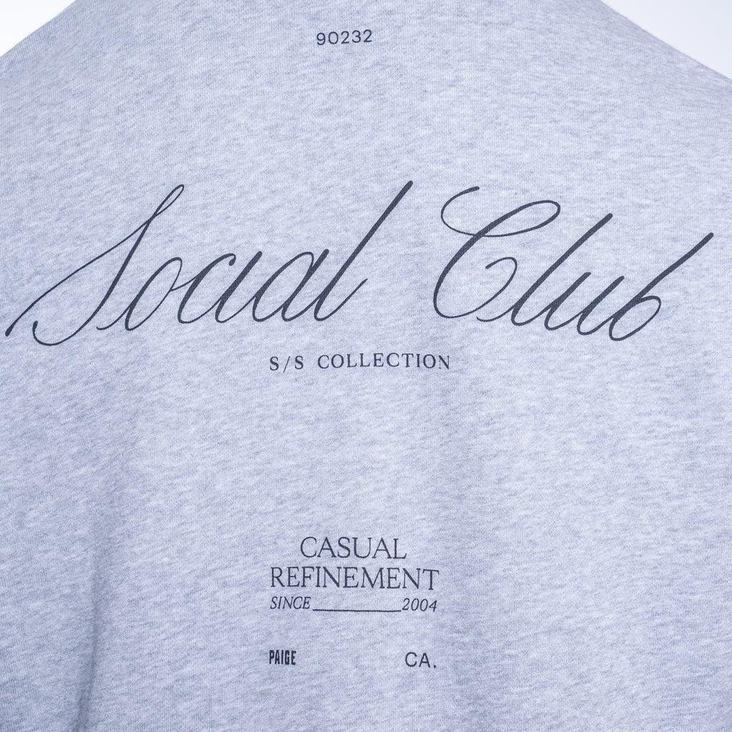 Close-up of a light heather gray t-shirt featuring black printed text on the front, including 'Social Club', 'S/S COLLECTION', and 'CASUAL REFINEMENT'. PAIGE Sweatshirt available at Sakks Menswear in Southampton.