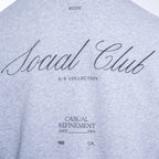 Close-up of a light heather gray t-shirt featuring black printed text on the front, including 'Social Club', 'S/S COLLECTION', and 'CASUAL REFINEMENT'. PAIGE Sweatshirt available at Sakks Menswear in Southampton.