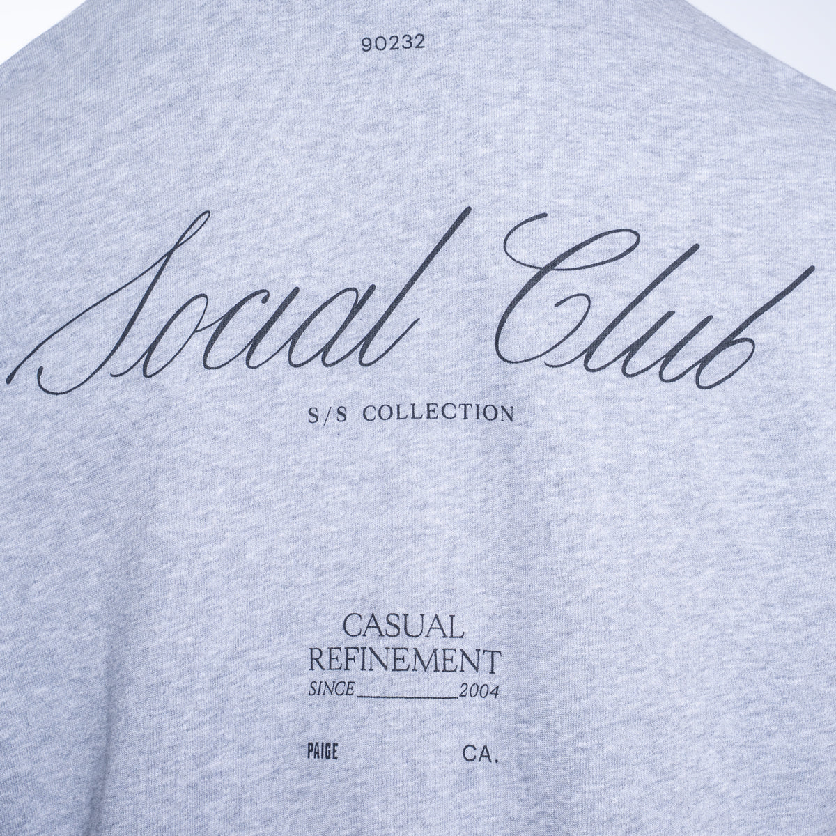 Close-up of a light heather gray t-shirt featuring black printed text on the front, including 'Social Club', 'S/S COLLECTION', and 'CASUAL REFINEMENT'. PAIGE Sweatshirt available at Sakks Menswear in Southampton.