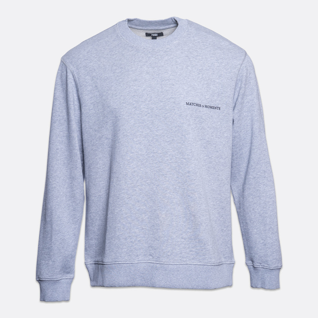 A light heather gray crewneck sweatshirt with 'MATCHES & MOMENTS' printed in black on the left chest, displayed on a clean white background. PAIGE Sweatshirt available at Sakks Menswear in Southampton.