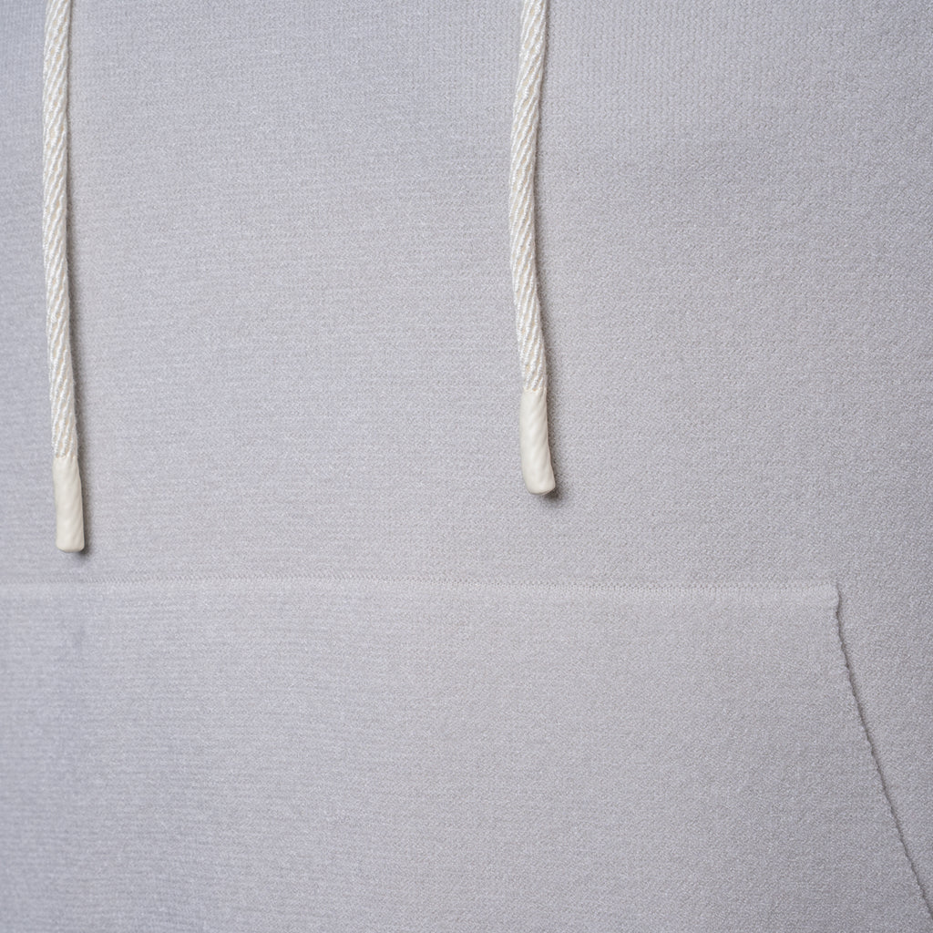 Close-up of a light gray hoodie showing the textured fabric and white drawstrings. PAIGE Hoodie available at Sakks Menswear in Southampton.