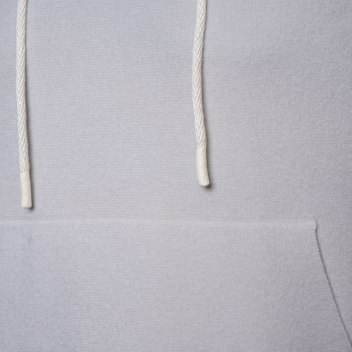 Close-up of a light gray hoodie showing the textured fabric and white drawstrings. PAIGE Hoodie available at Sakks Menswear in Southampton.