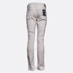 A pair of slim-fit jeans shown from the back, in a light beige or sand color, featuring a dark blue brand patch on the right back pocket, set against a plain light gray background. PAIGE Jeans available at Sakks Menswear in Southampton.