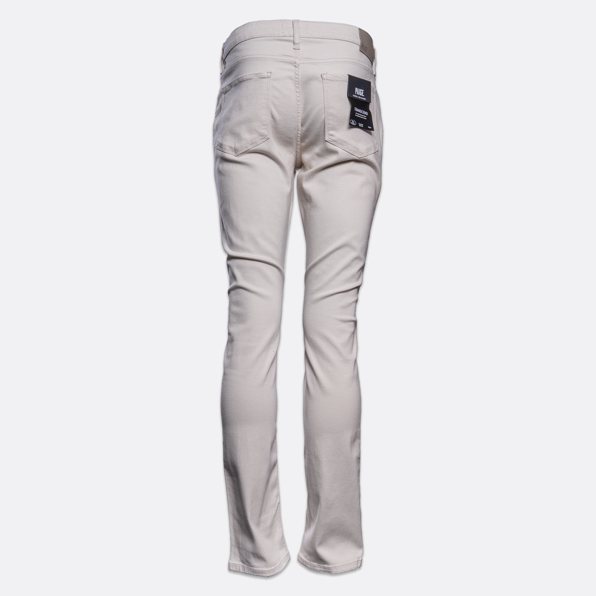 A pair of slim-fit jeans shown from the back, in a light beige or sand color, featuring a dark blue brand patch on the right back pocket, set against a plain light gray background. PAIGE Jeans available at Sakks Menswear in Southampton.