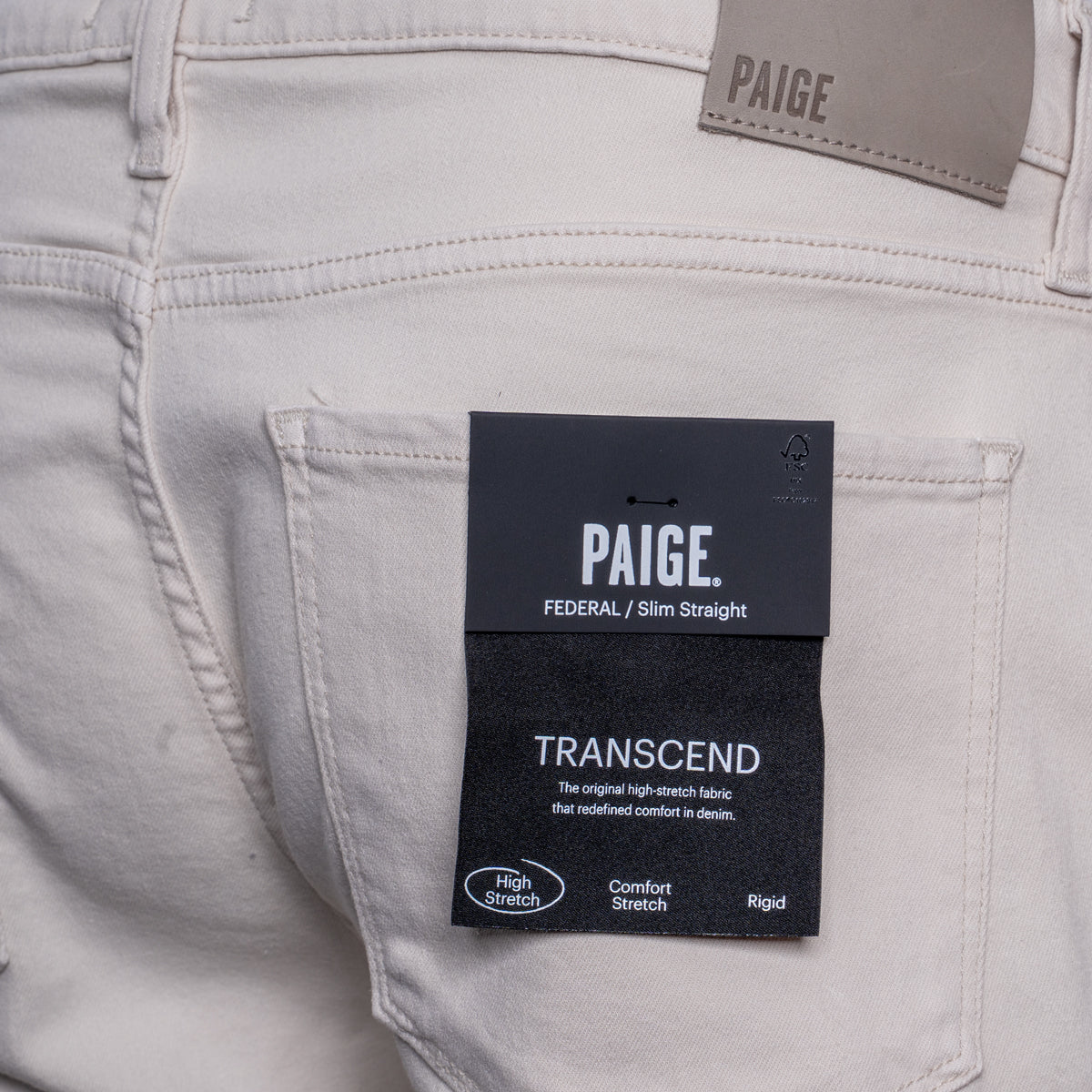 Close-up of the back pocket of light beige denim jeans with a black PAIGE Transcend label attached to the back pocket. PAIGE Jeans available at Sakks Menswear in Southampton.