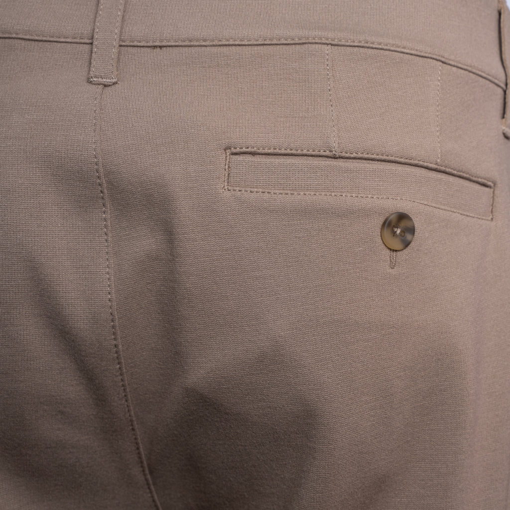 Close-up of the back waistband and pocket area of light beige trousers, showing a buttoned welt pocket and belt loop. PAIGE Trousers available at Sakks Menswear in Southampton.