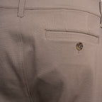 Close-up of the back waistband and pocket area of light beige trousers, showing a buttoned welt pocket and belt loop. PAIGE Trousers available at Sakks Menswear in Southampton.
