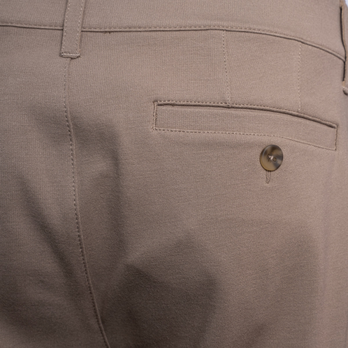 Close-up of the back waistband and pocket area of light beige trousers, showing a buttoned welt pocket and belt loop. PAIGE Trousers available at Sakks Menswear in Southampton.