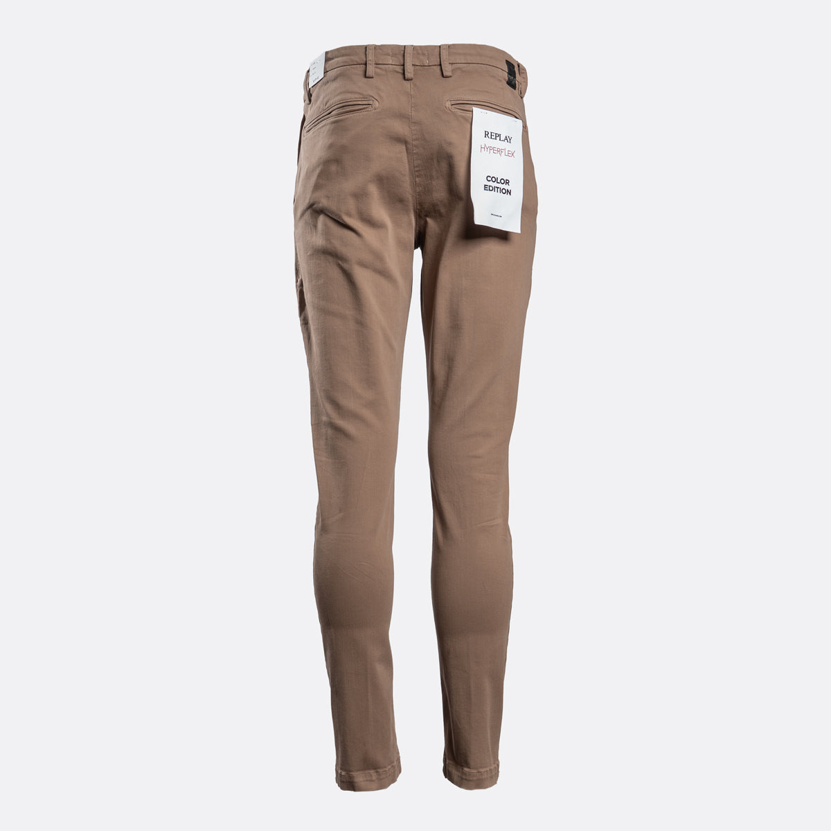 A pair of slim-fit brown pants shown from the back, featuring a white paper tag attached to the back pocket, set against a plain light gray background. Replay Chino available at Sakks Menswear in Southampton.
