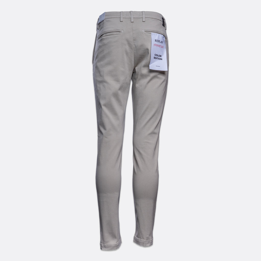 A pair of light gray slim-fit pants shown from the back, featuring a white paper tag attached to the back pocket, set against a plain light gray background. Replay Chinos available at Sakks Menswear in Southampton.