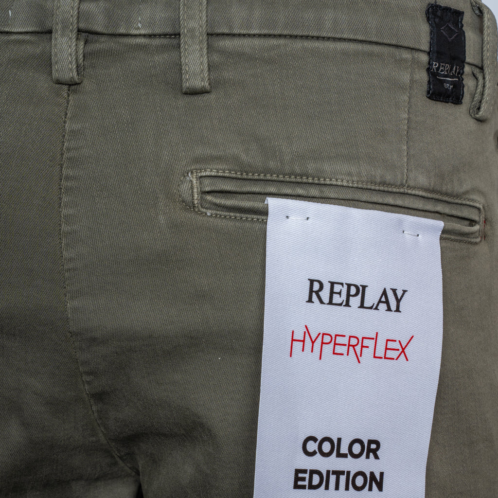 Close-up of the back waistband and pocket area of olive green Replay Hyperflex pants, with a white paper hangtag reading 'REPLAY HYPERFLEX COLOR EDITION' attached near the pocket. Replay Shorts available at Sakks Menswear in Southampton.