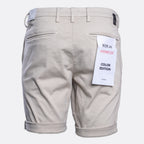 Back view of light beige chino shorts with rolled cuffs, featuring a white paper tag on the right pocket that reads 'REPLAY HYPERFLEX COLOR EDITION'. Replay Shorts available at Sakks Menswear in Southampton.