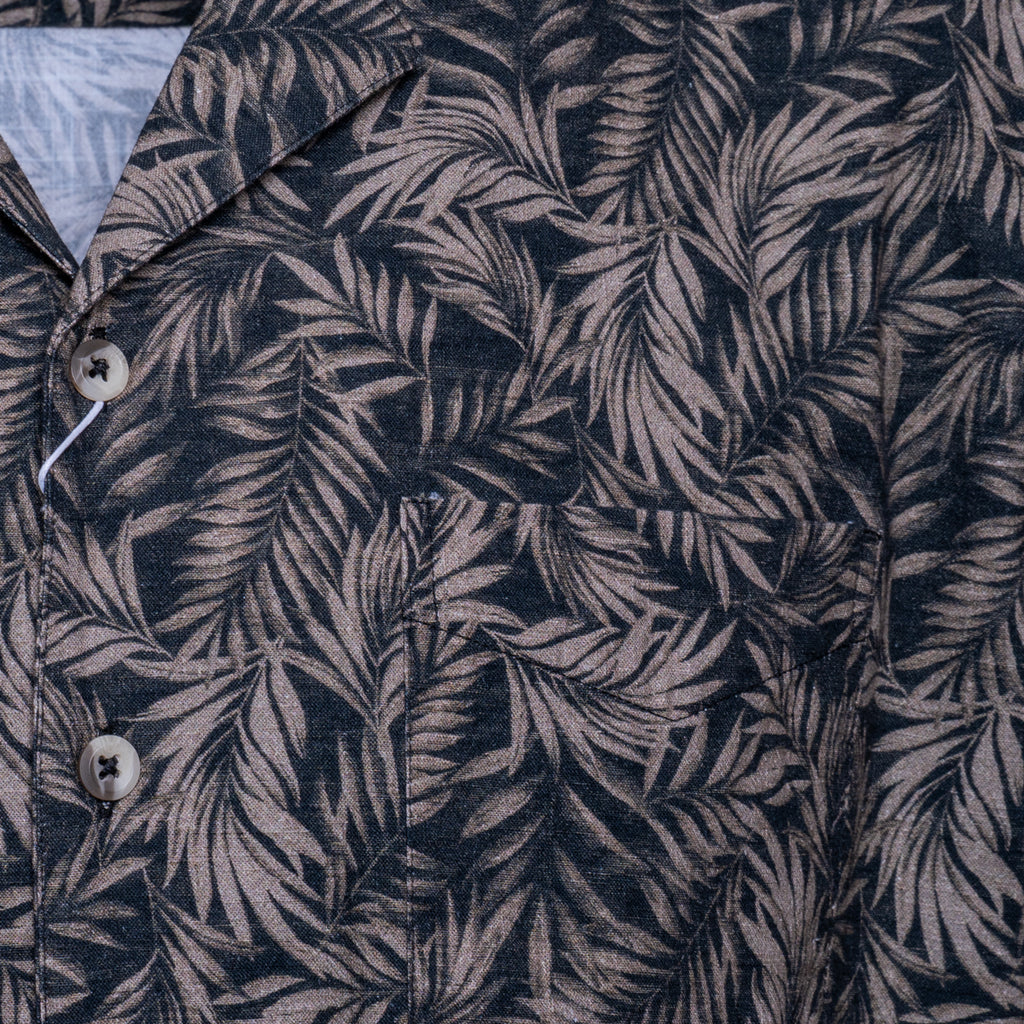 Close-up of a button-front shirt with an allover tropical leaf print in dark navy and muted taupe-gray. Sand Copenhagen Short Sleeve Shirt available at Sakks Menswear in Southampton.
