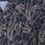 Close-up of a button-front shirt with an allover tropical leaf print in dark navy and muted taupe-gray. Sand Copenhagen Short Sleeve Shirt available at Sakks Menswear in Southampton.