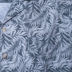 Close-up of a button-front shirt with a gray and white tropical palm leaf pattern, showing part of the collar and two light-colored buttons. Sand Copenhagen Short Sleeve Shirt available at Sakks Menswear in Southampton.