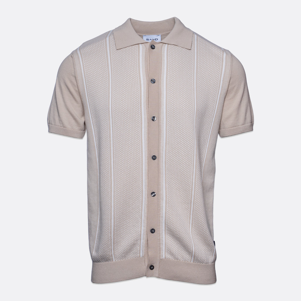 A short-sleeve knit polo shirt in a light beige color, featuring vertical textured stripes and a button-up front, shown against a plain light gray background. Sand Copenhagen Polo available at Sakks Menswear in Southampton.