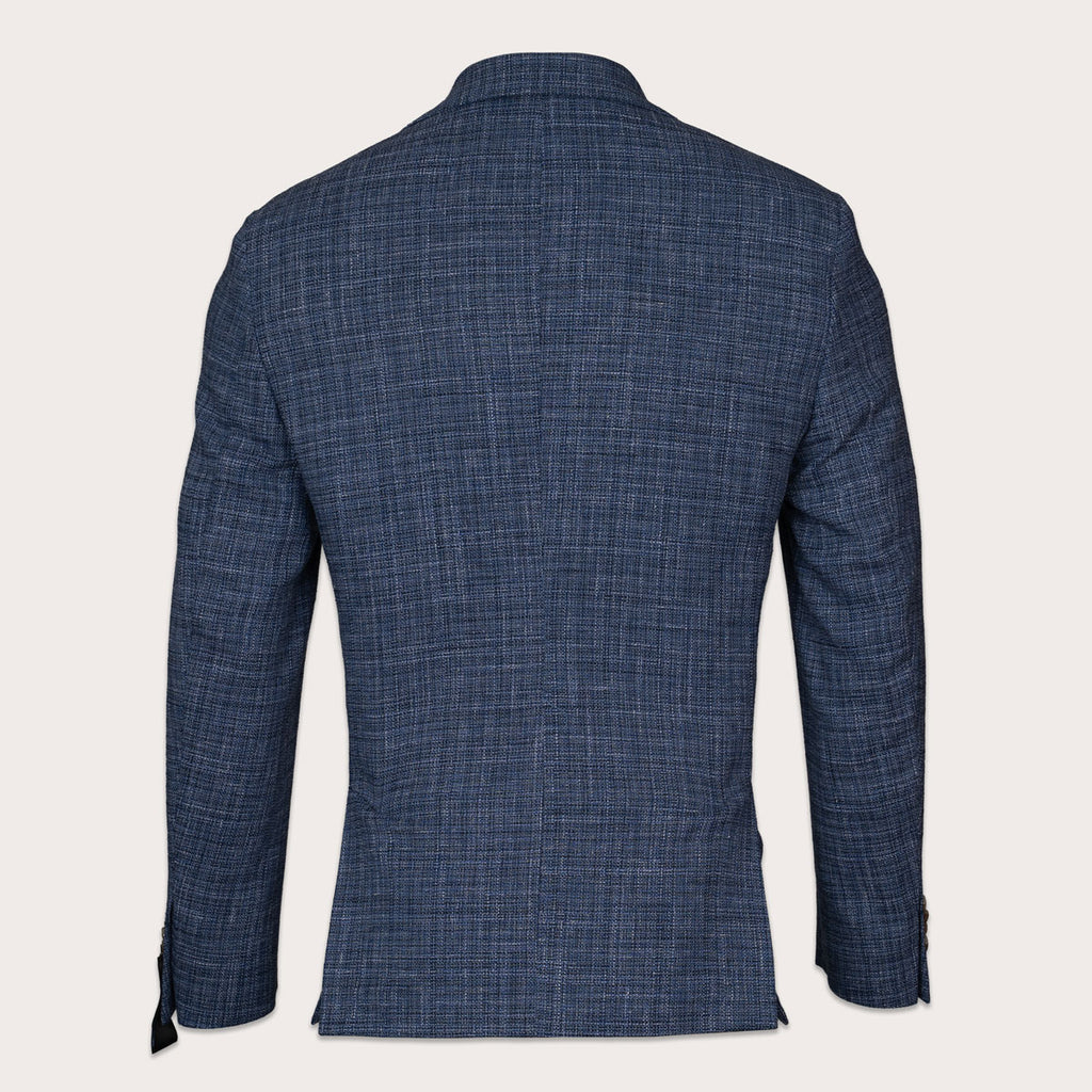 A men's navy blue textured blazer shown from the back, featuring a subtle woven grid pattern and a classic collar, set against a solid off-white background. Sand Copenhagen Blazers available at Sakks Menswear in Southampton.