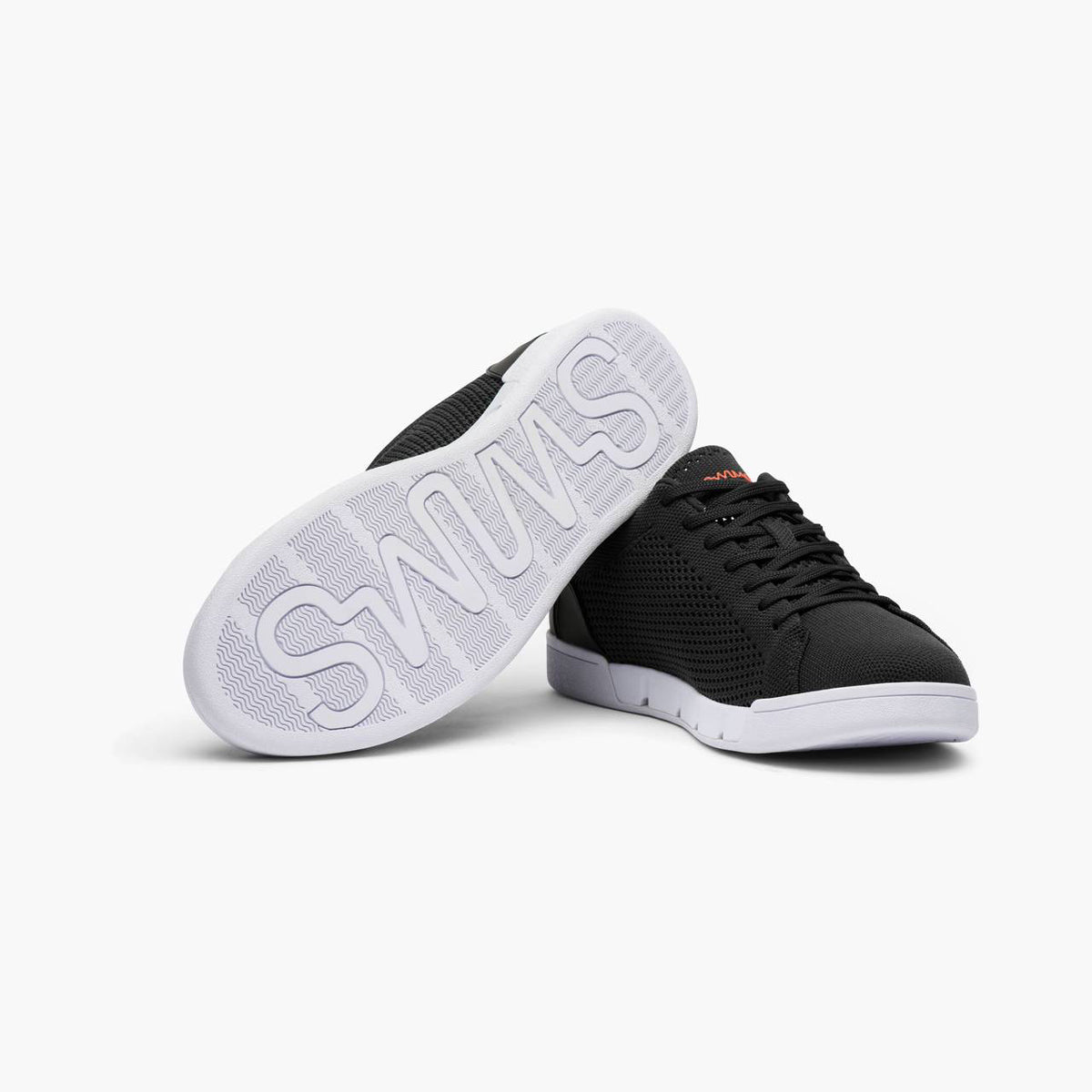 A pair of black low-top sneakers with white soles, one shown from the side and the other from the bottom to display the large 'SNEAKS' branding on the outsole. SWIMS Sneakers available at Sakks Menswear in Southampton.
