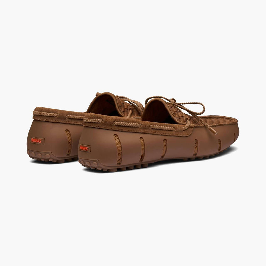 A pair of brown suede moccasin-style driving shoes with matching brown laces, shown from a three-quarters rear angle on a light gray background. SWIMS Loafers available at Sakks Menswear in Southampton.