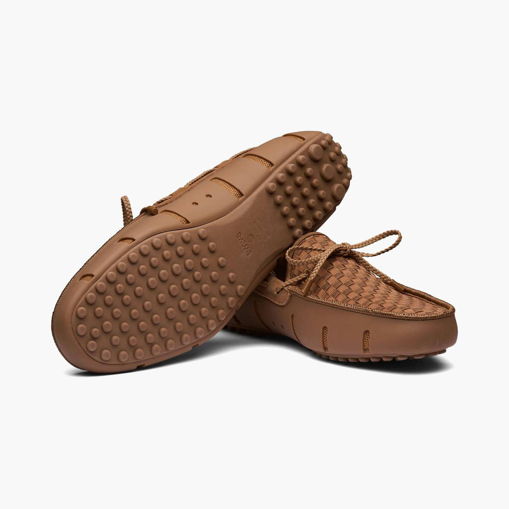 A pair of brown woven slip-on moccasin-style shoes with a textured, raised sole, shown on a clean white background. SWIMS Loafers available at Sakks Menswear in Southampton.