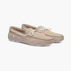 A pair of beige slip-on moccasin-style shoes with white laces and light pink stitching accents, shown on a clean white background. SWIMS Loafers available at Sakks Menswear in Southampton.