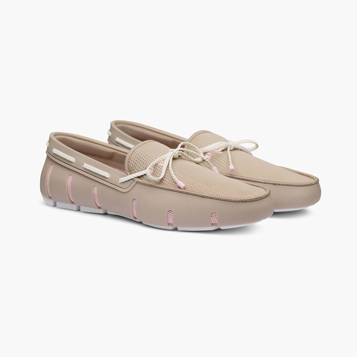 A pair of beige slip-on moccasin-style shoes with white laces and light pink stitching accents, shown on a clean white background. SWIMS Loafers available at Sakks Menswear in Southampton.