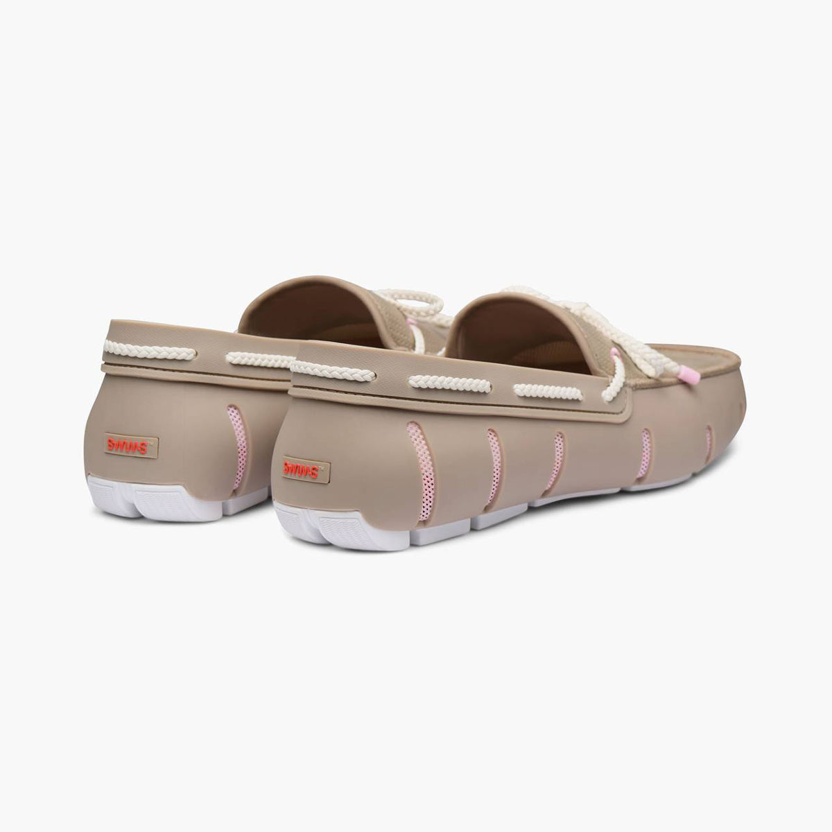 A pair of beige slip-on clogs with white rope-style trim and pink stitching details, shown from a three-quarters angle on a light gray background. SWIMS Loafers available at Sakks Menswear in Southampton.