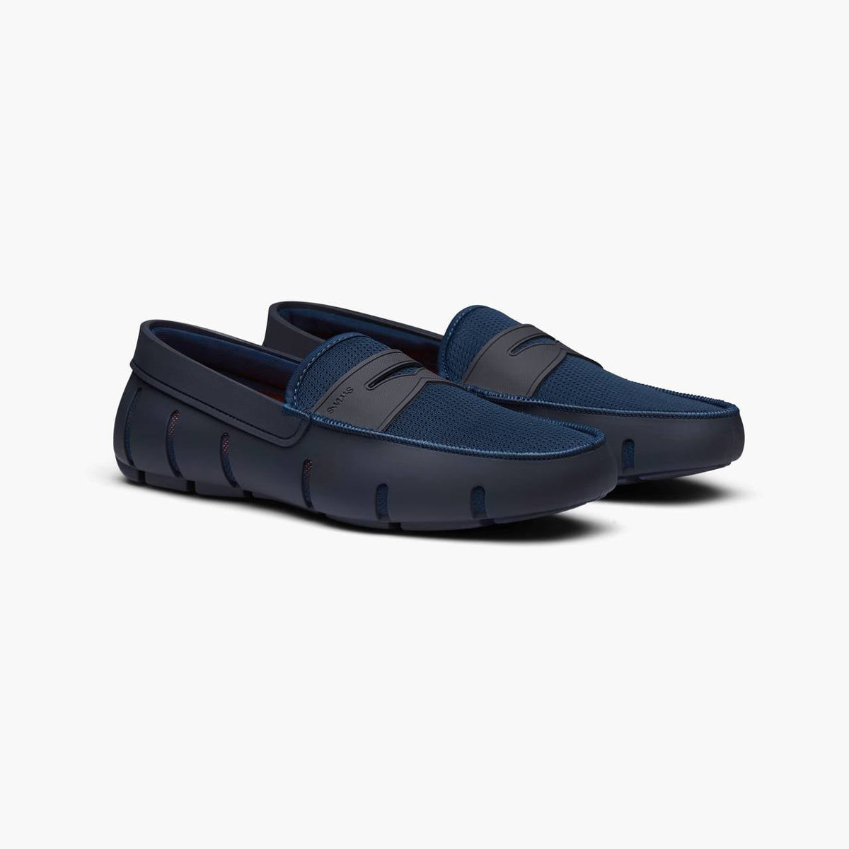 A pair of navy blue slip-on loafers with a textured mesh upper and a thick, sculpted sole, shown on a light gray background. SWIMS Loafers available at Sakks Menswear in Southampton.