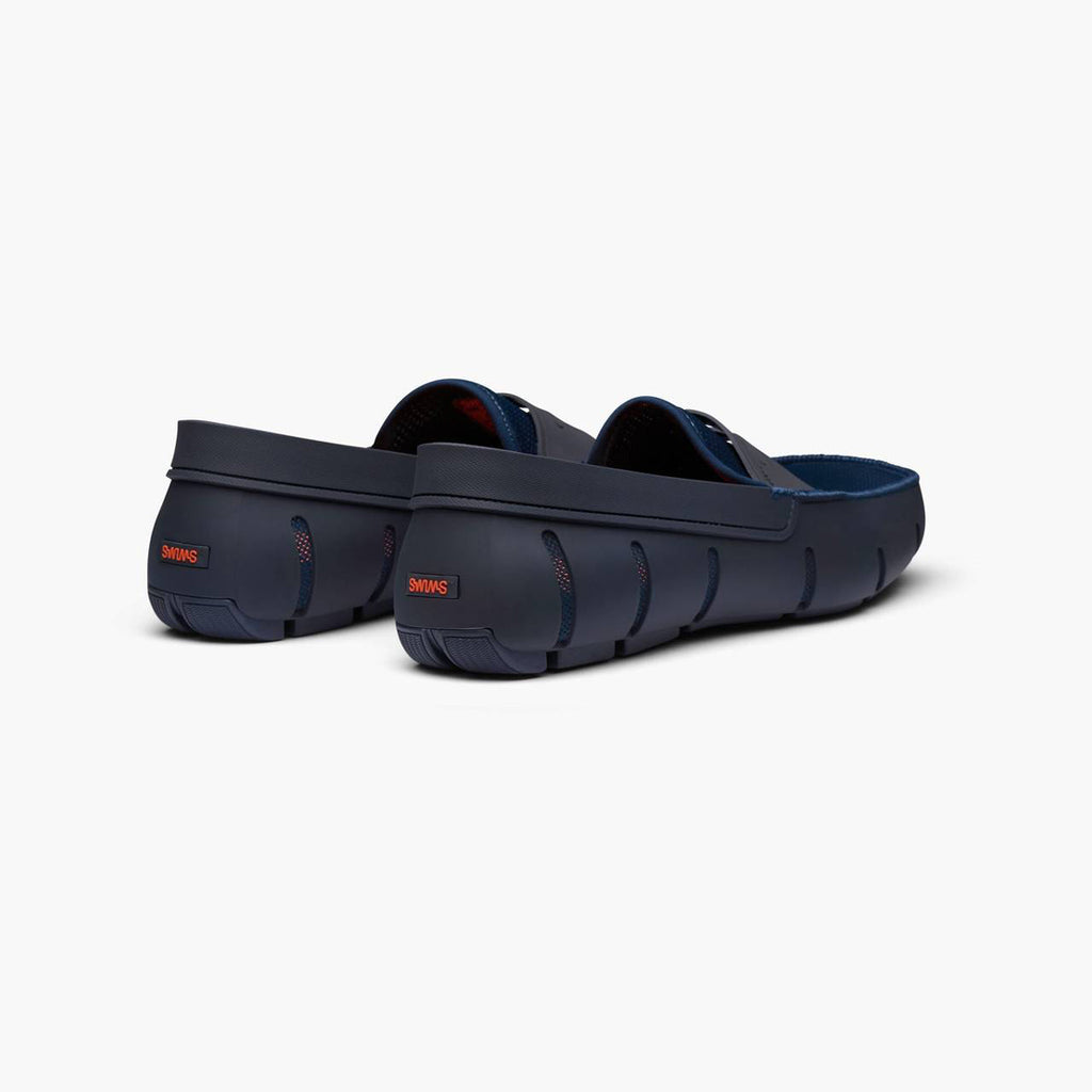 A pair of navy blue Crocfoot clogs shown from a three-quarters rear angle on a clean, light gray background. SWIMS Loafers available at Sakks Menswear in Southampton.