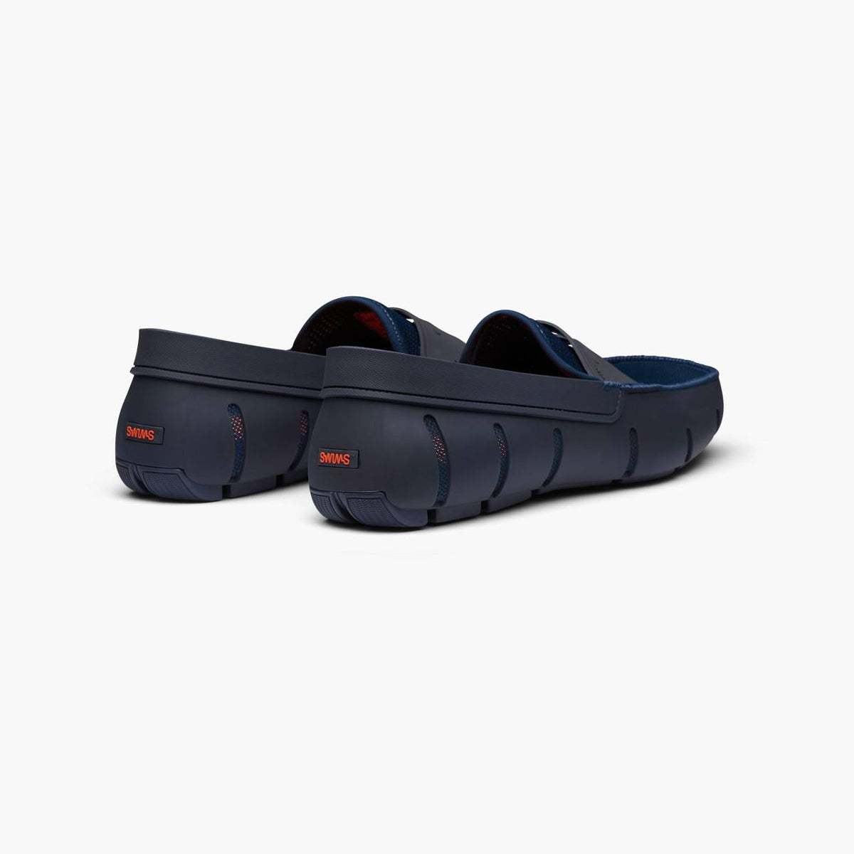 A pair of navy blue Crocfoot clogs shown from a three-quarters rear angle on a clean, light gray background. SWIMS Loafers available at Sakks Menswear in Southampton.