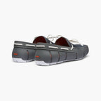 A pair of dark gray slip-on boat shoes with white laces, white stitching, and white soles, shown from a three-quarters rear angle on a light gray background. SWIMS Loafers available at Sakks Menswear in Southampton.