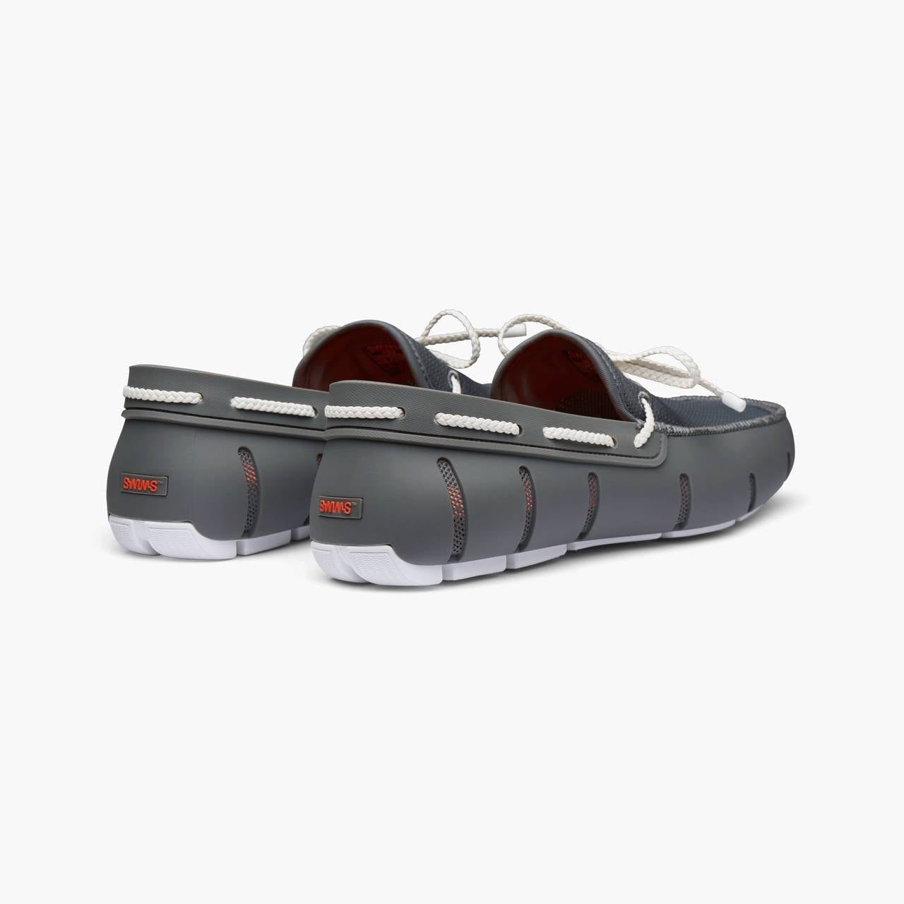 A pair of dark gray slip-on boat shoes with white laces, white stitching, and white soles, shown from a three-quarters rear angle on a light gray background. SWIMS Loafers available at Sakks Menswear in Southampton.