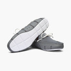 A pair of gray slip-on boat shoes with white laces, shown from a three-quarters perspective to display both the side profile and the textured white outsole. SWIMS Loafers available at Sakks Menswear in Southampton.