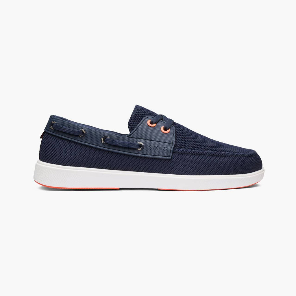 A navy blue boat shoe with a white sole and orange eyelets, shown in a side profile on a light gray background. SWIMS Boat Shoes available at Sakks Menswear in Southampton.