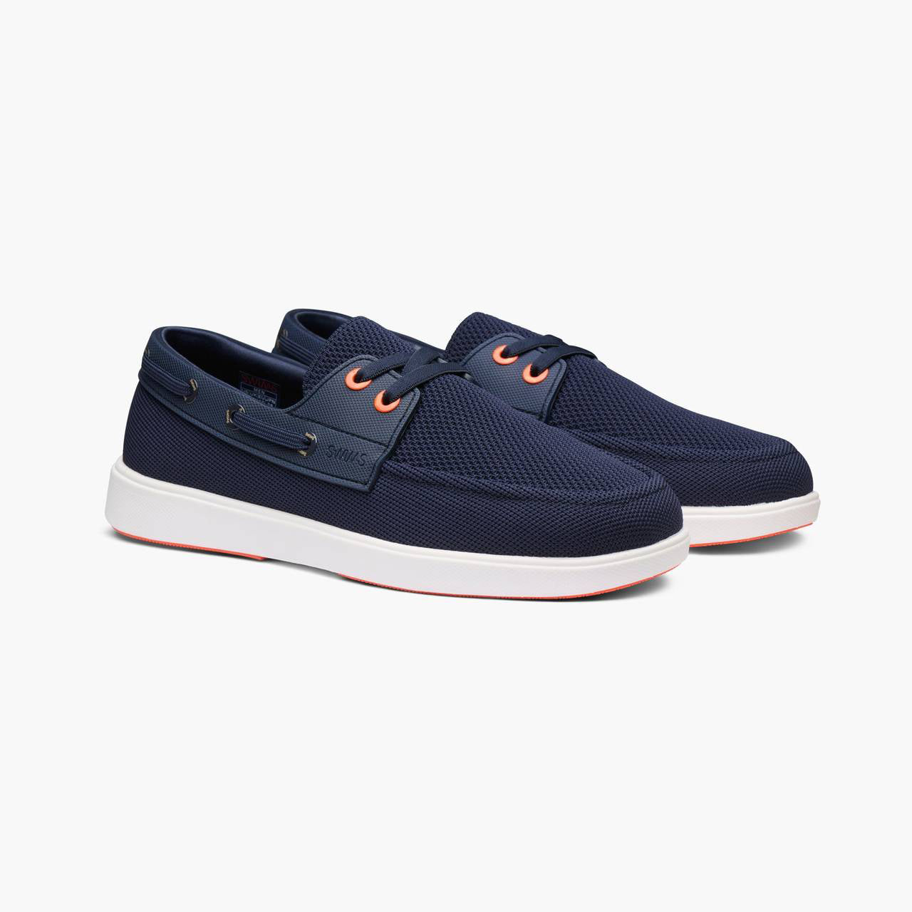 A pair of navy blue mesh boat shoes with white soles and orange eyelets, shown on a light gray background. SWIMS Boat Shoes available at Sakks Menswear in Southampton.