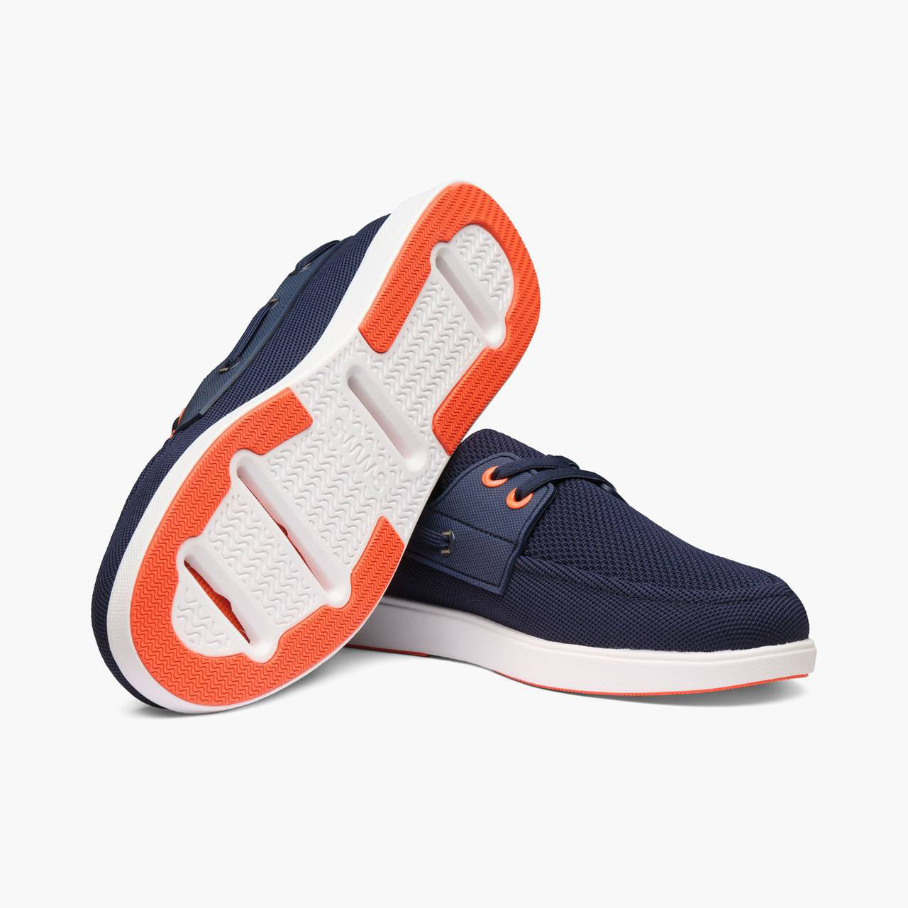 A pair of navy blue mesh boat-style sneakers with white and bright orange soles, shown on a clean white background. SWIMS Boat Shoes available at Sakks Menswear in Southampton.