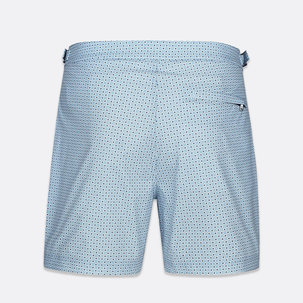 Light blue swim trunks with a small dark blue geometric pattern, featuring a side pocket and a waistband with side tabs, shown against a light gray background. SWIMS Swim Shorts available at Sakks Menswear in Southampton.