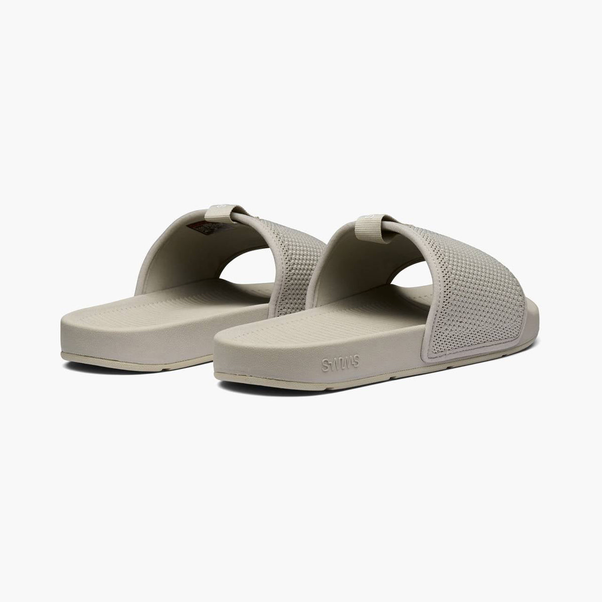A pair of light gray slide sandals with perforated straps and a thick cushioned sole, shown from a three-quarters angle on a light gray background. SWIMS Slides available at Sakks Menswear in Southampton.